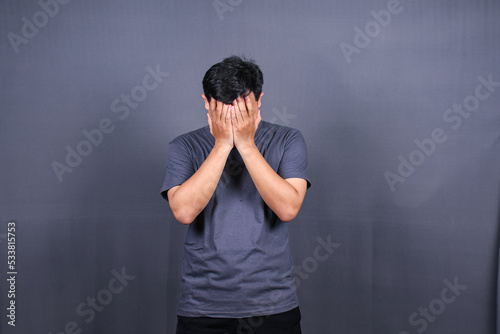 Depressed Asian Young man having stressful time with hands covering face. isolated on gray background. 