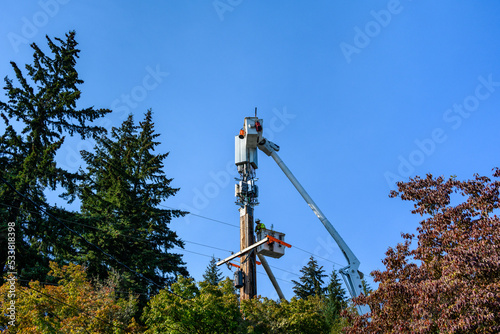 Two linemen working on a wireless communications radio and antenna installation using a bucket truck 