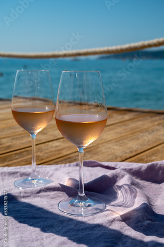 Glasses of cold rose wine from Provence served outdoor on wooden yacht pier with view on blue water and white sandy beach Plage de Pampelonne near Saint-Tropez, France