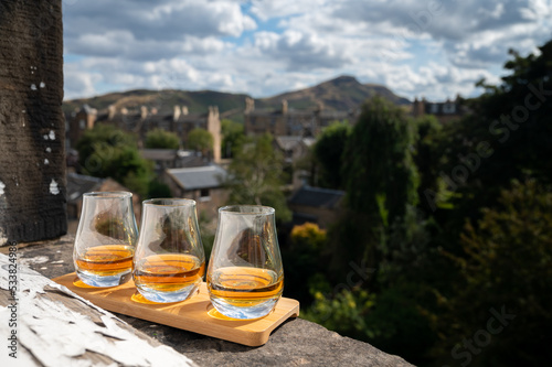 Flight of single malt scotch whisky served on old window sill in Scottisch house with view on old part of Edinburgh and hills, Scotland, UK photo