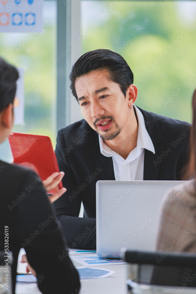 Millennial Asian professional successful bearded male businessman manager in formal suit sitting smiling working with tablet computer discussing with colleague in company office meeting room Millennial Asian professional successful bearded male businessman manager in formal suit sitting smiling working with tablet computer discussing with colleague in company office meeting room