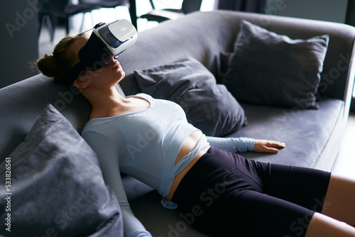 Robot like futuristic doll woman in virtual reality goggles interface on head enters metaverse immersive experience via headset. Creepy looking satisfaction girl in depression after cyber space. photo