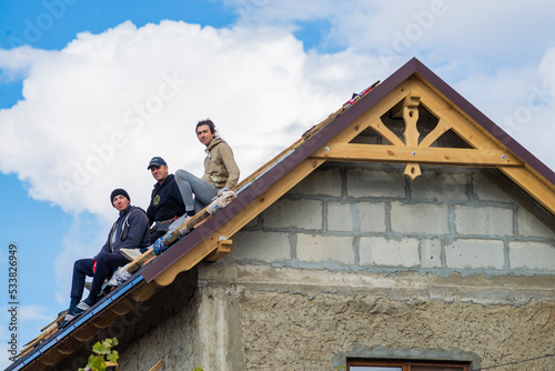three Roofer man roof carpenter working Country house renovation. looking at camera blue sky beautiful clouds  unfinished wall  concrete block