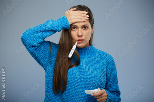 Sick woman with fever touching her forehead holding thermometer. isolated portrait female person with eyes closed. photo