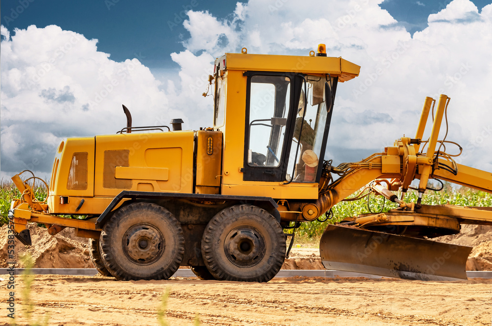 Road grader at the construction site. Powerful construction machine for ground leveling and excavation. Close-up. Professional construction equipment.