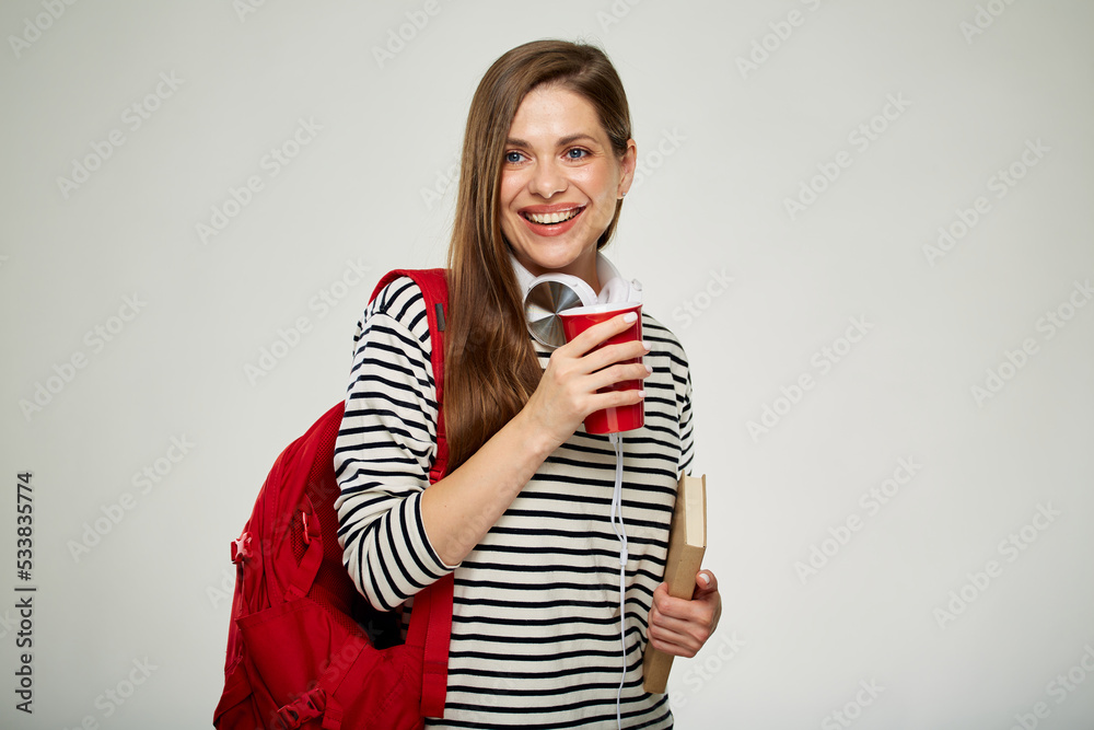 Obraz premium Smiling student woman looking away standing with book and red backpack holding coffee cup. isolated female portrait on white background.