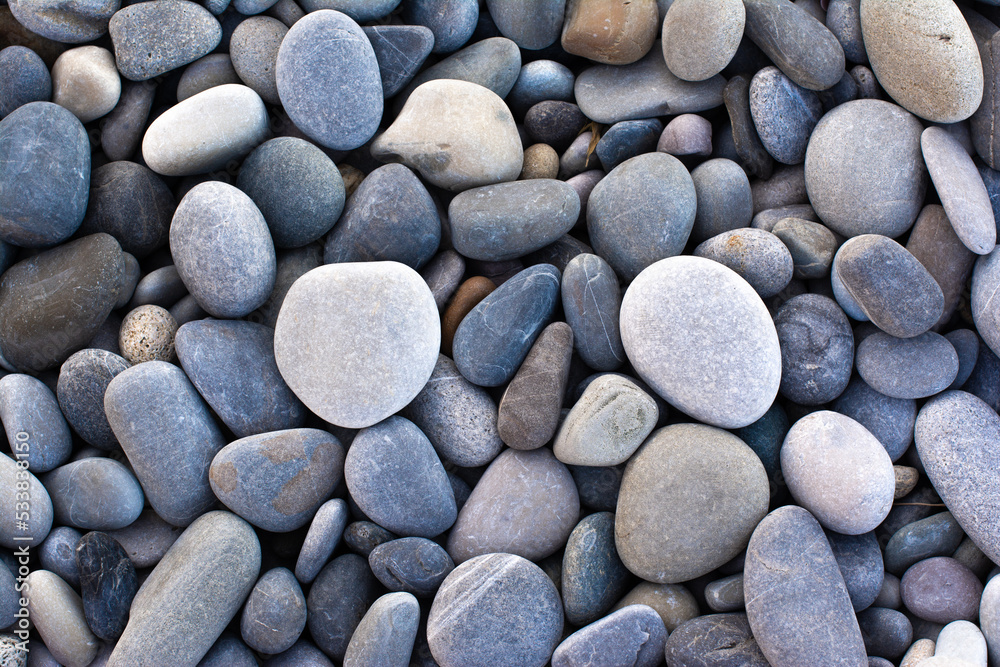 Abstract background with round pebble stones. Stones beach smooth. Top view. Summer day. Close-up. Flat lay texture in daylight. Abstract background with round pebble stones. Stones beach smooth. Top view. Summer day. Close-up. Flat lay texture in daylight.