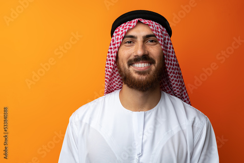 Portrait of young smiling Arab man on orange background