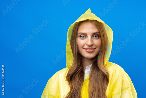Canvastavla Young blonde woman wearing yellow raincoat smiling at camera over blue backgroun