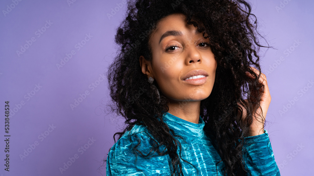 African american confident woman in velvet dress with wavy hair posing on blue violet background. Fashion style studio portrait. African american confident woman in velvet dress with wavy hair posing on blue violet background. Fashion style studio portrait.