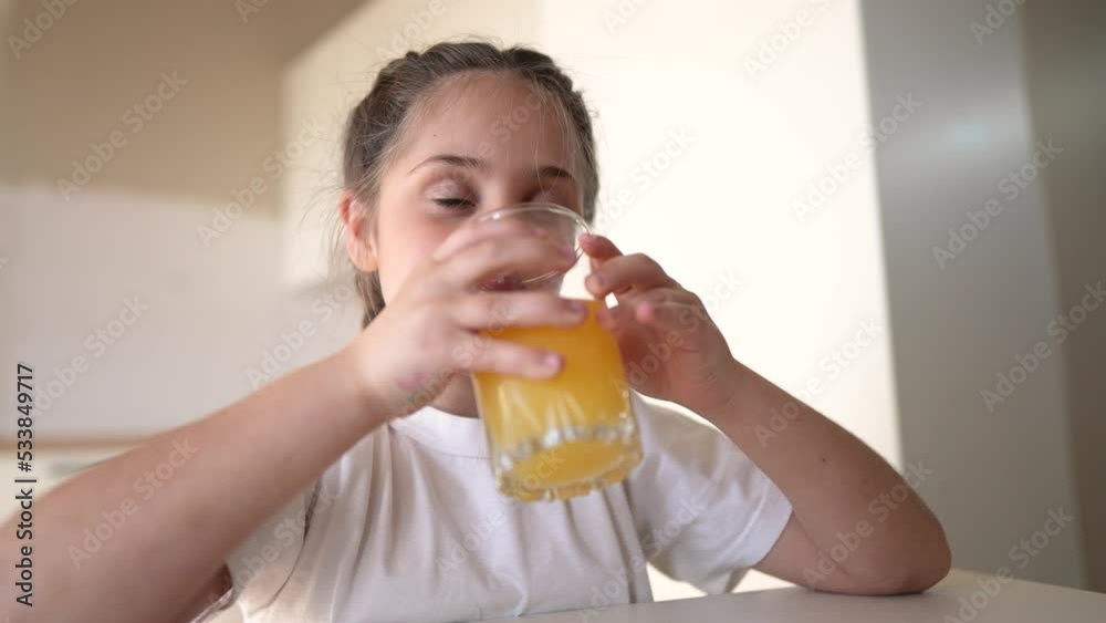 girl child drinking juice. happy family a healthy eating kid dream concept. daughter girl drinking yellow juice from a glass cup in indoors the kitchen. child drinking fruit juice girl child drinking juice. happy family a healthy eating kid dream concept. daughter girl drinking yellow juice from a glass cup in indoors the kitchen. child drinking fruit juice