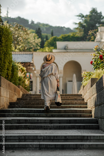 Woman on the stairs in the park. A middle-aged lady in a hat in a white outfit with a bag walks around the Livadia Palace © svetograph