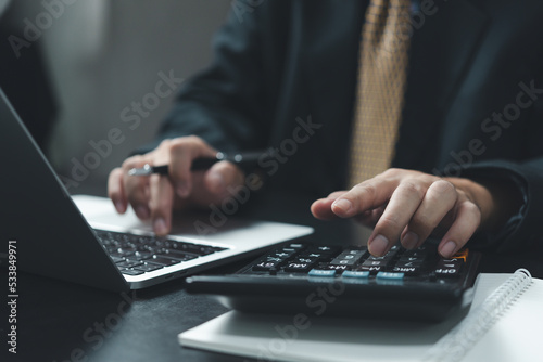 Business man hand using calculator holding pen and with doing finance and tax accounting on desk at home office.