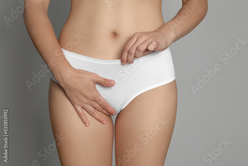 Woman suffering from genital herpes on light grey background, closeup photo