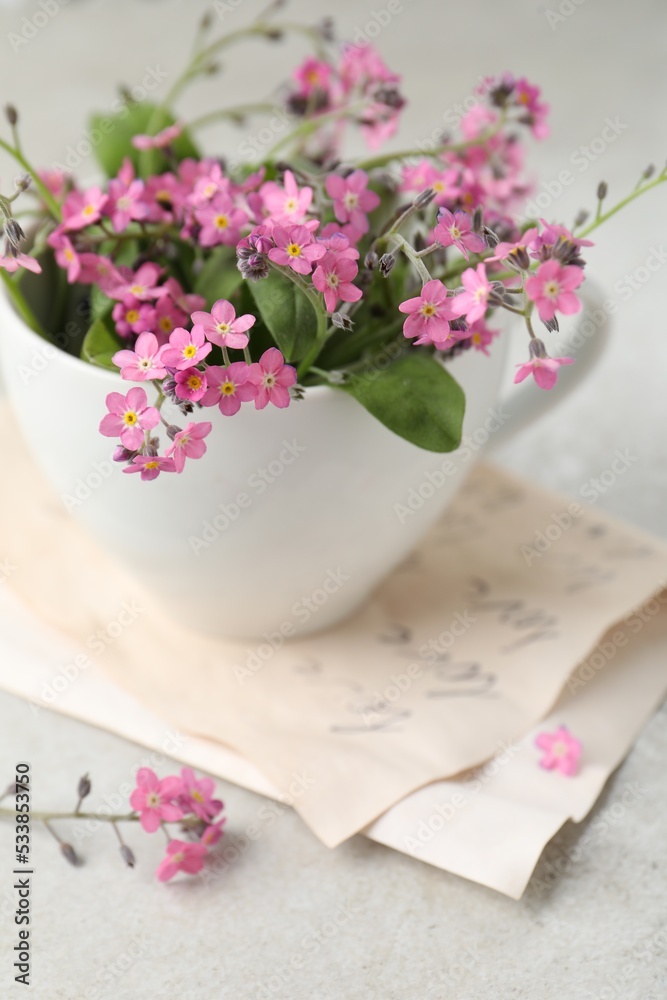 Beautiful pink forget-me-not flowers with cup on light stone table, closeup