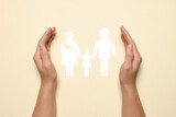 Woman holding hands around paper silhouette of family on beige background, top view. Insurance concept