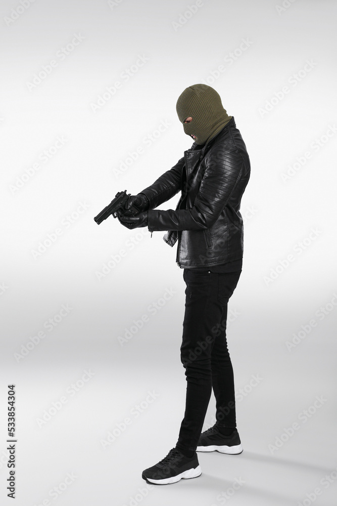 Man wearing knitted balaclava with gun on light grey background Man wearing knitted balaclava with gun on light grey background