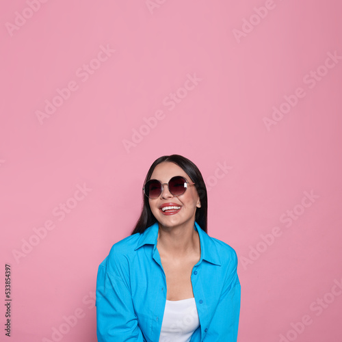 Attractive happy woman in fashionable sunglasses against pink background