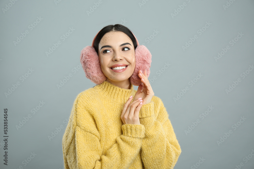 Beautiful young woman wearing earmuffs on light grey background