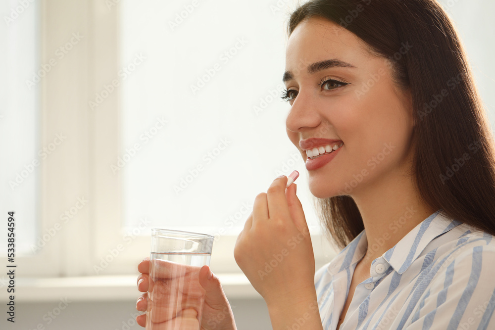 Young woman with glass of water taking dietary supplement pill indoors, space for text Young woman with glass of water taking dietary supplement pill indoors, space for text