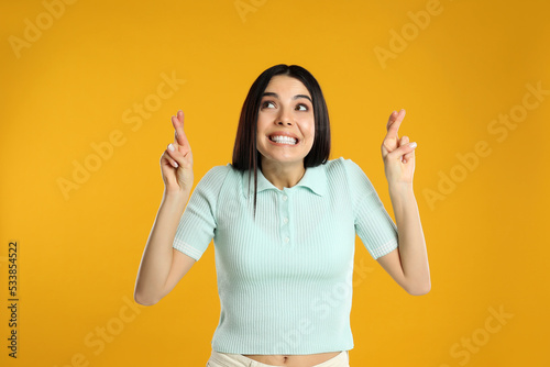 Woman with crossed fingers on yellow background. Superstition concept