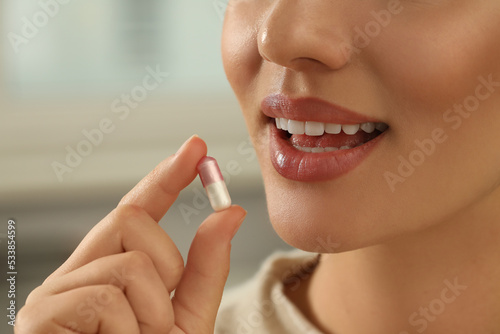 Young woman taking dietary supplement pill on blurred background, closeup photo