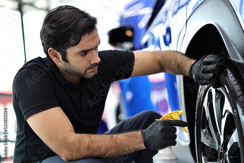 Car service worker polishing car wheels with microfiber cloth and waxing tire of car.