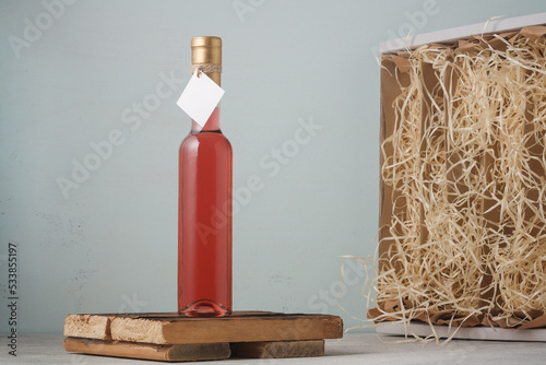 Bottle of pink wine with mock up blank label, no brand template, box with decoratives havings filler on wooden background