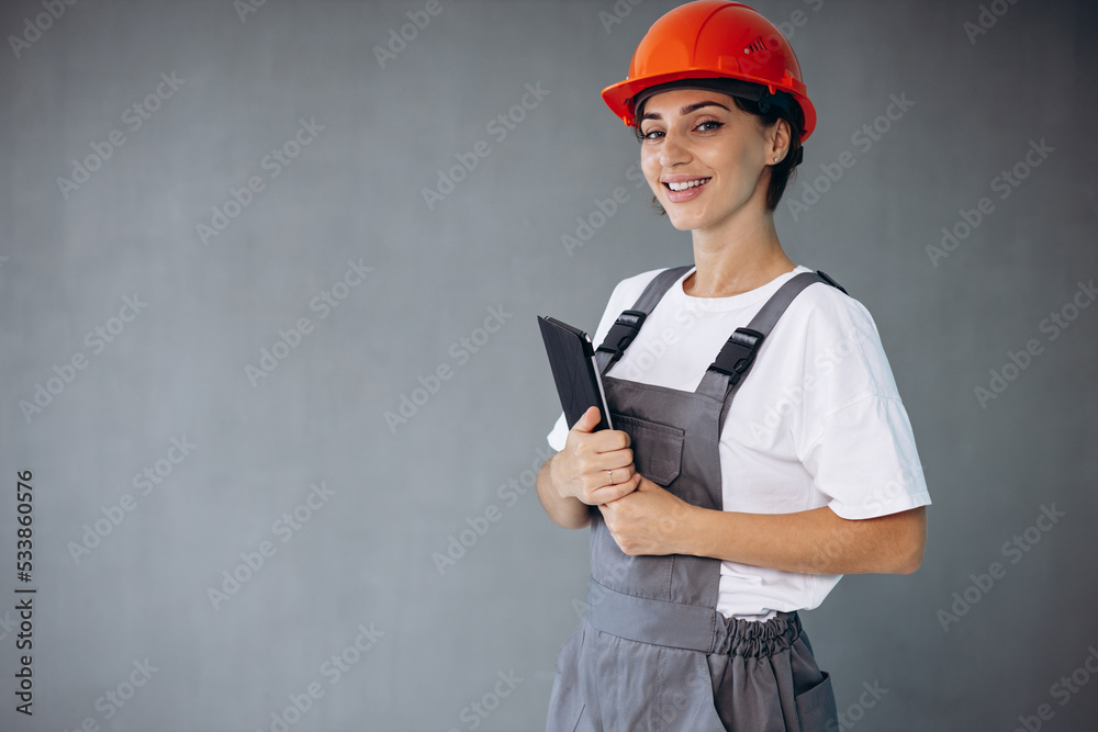 Woman builder in helmet wearing grey overalls holding tablet Woman builder in helmet wearing grey overalls holding tablet