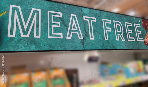 Close up color image depicting a Meat Free sign indicating the vegetarian food section inside a supermarket. Focus is on the sign, while the aisle of the supermarket is entirely defocused. photo