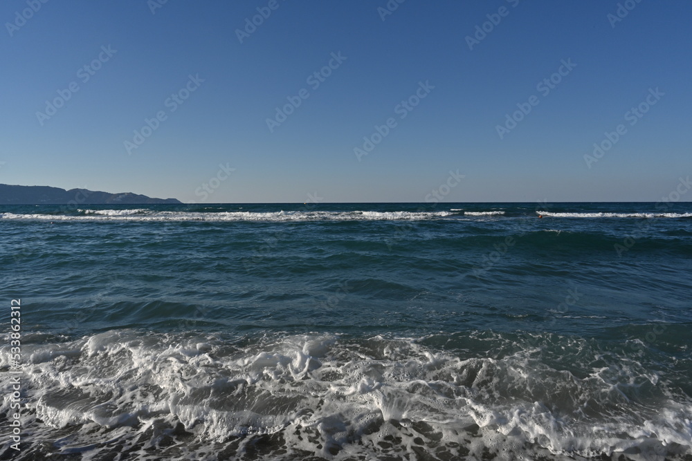Waves on the Sea of Crete. There is splashed water on the crest of the wave. Suitable as background, abstract and texture. In horizon is mountain coast of Greek island Creta during summer time.
