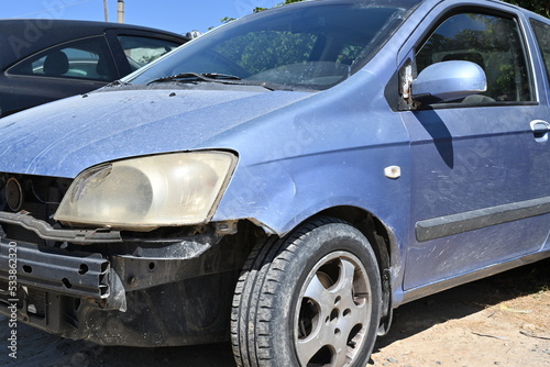 View on car damages in front part of the vehicle. Fender, halogen light and door back mirror are broken, their position is shifted and the paint is scratched. Forward plastic bumper is missing.