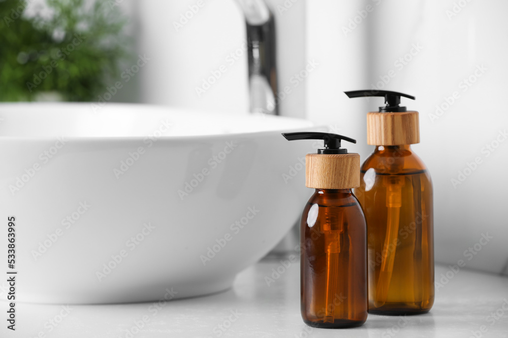 Bottles with dispenser caps on white table in bathroom. Space for text Bottles with dispenser caps on white table in bathroom. Space for text