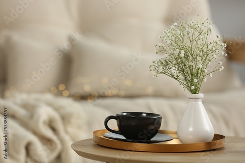 Vase with hypsophila and cup on round wooden table in living room