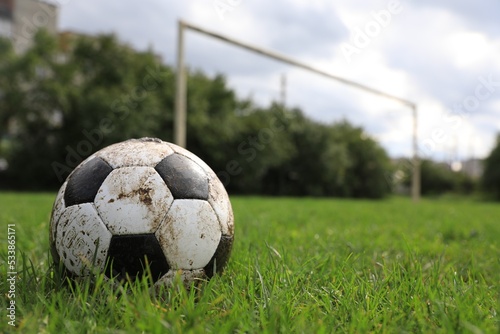 Dirty soccer ball on green grass outdoors, space for text