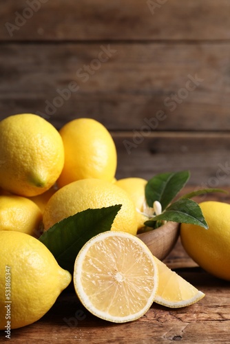 Many fresh ripe lemons with green leaves on wooden table
