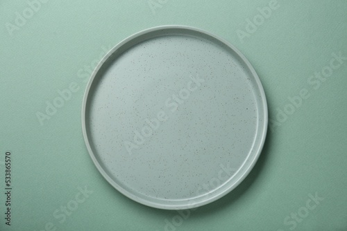Empty ceramic plate on green background, top view