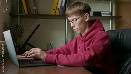 Young guy, typing on laptop, copying text from notes, working, studying remotely