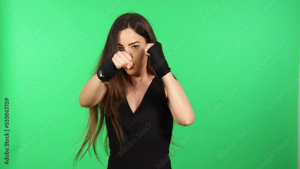 Sportswoman punching looking at camera with boxing hand wraps and green screen in background Sportswoman punching looking at camera with boxing hand wraps and green screen in background
