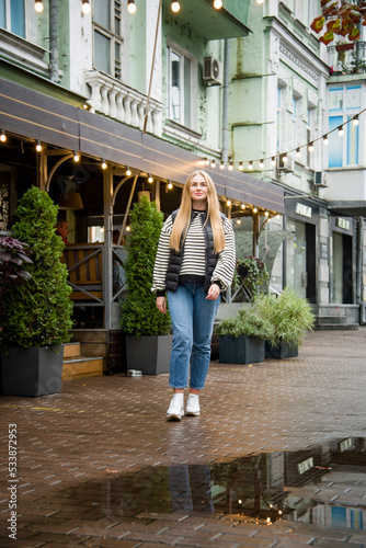 smiling woman with long blond hair in jeans walking on the street