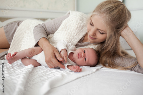 A young and beautiful mother is holding a newborn baby in her arms, taking care of him at home.