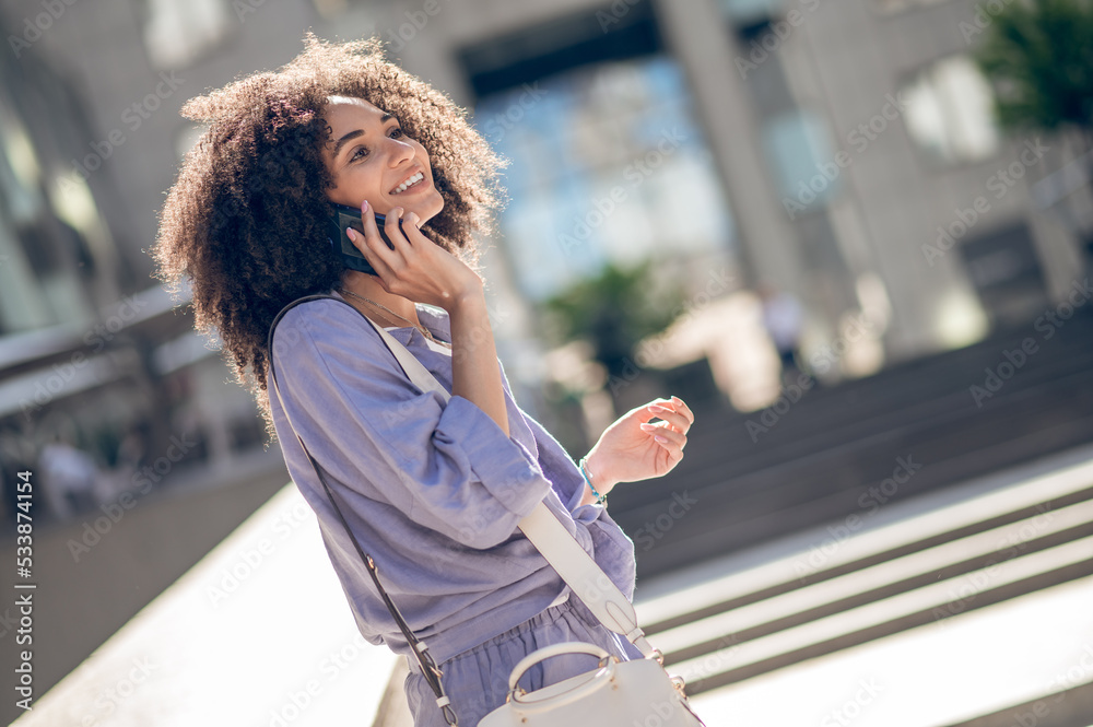 Cute young curly-haired woman talking on the phone