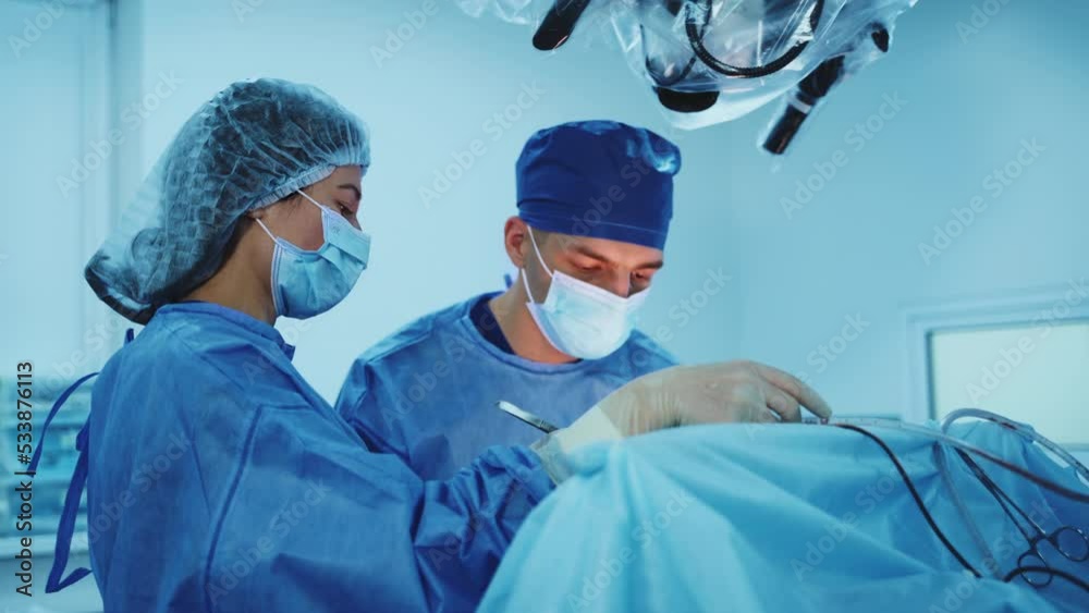 Doctor concentrated on his work at operation. Female nurse assisting the surgeon using metal tools and instruments. Doctor concentrated on his work at operation. Female nurse assisting the surgeon using metal tools and instruments.