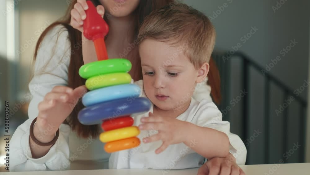 the child collects a toy pyramid. mom plays with son at home happy family. development of fine motor skills in a newborn child. happy family mom fun and baby play pyramid game. preschool education the child collects a toy pyramid. mom plays with son at home happy family. development of fine motor skills in a newborn child. happy family mom fun and baby play pyramid game. preschool education