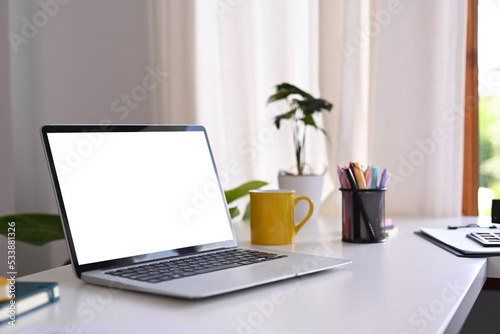 White office desk with laptop computer, coffee cup, potted plant and stationery. Comfortable workplace