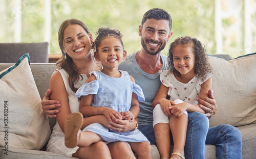 Happy, smile and portrait of a family bonding in the living room to relax on the sofa together. Happiness, care and parents sitting and holding their girl children with love on a couch at home.