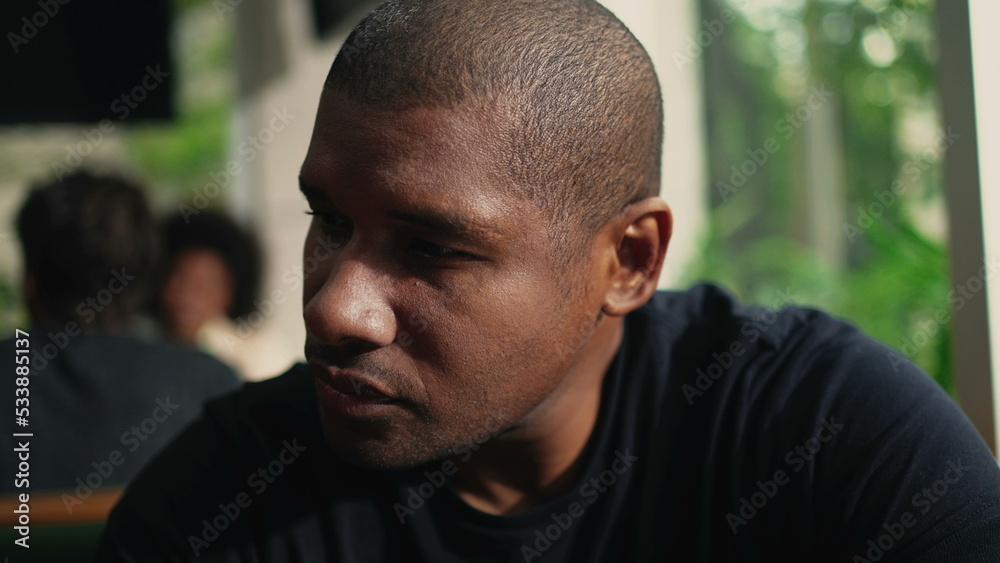 One young black man in dramatic look seated at coffee shop with contrast shadows by the window One young black man in dramatic look seated at coffee shop with contrast shadows by the window