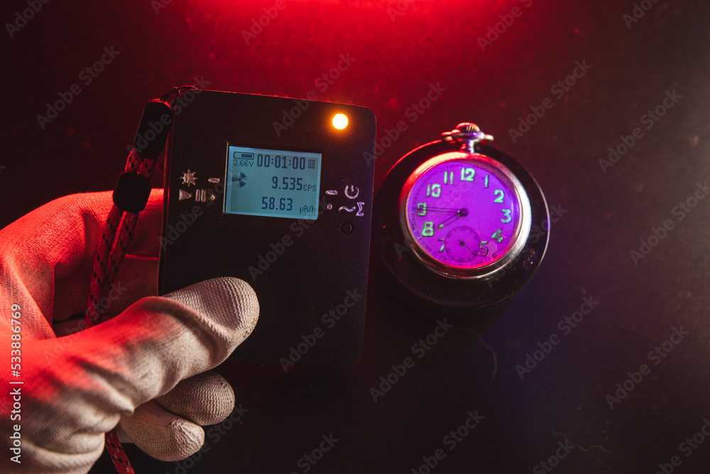 Man hand use dosimeter of radioactive radiation next to an old pocket watch with dangerous