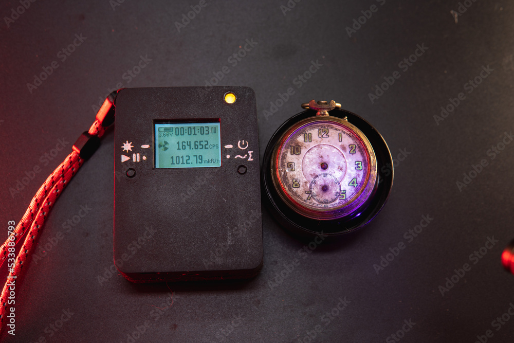 Dosimeter of radioactive radiation and old broken pocket watch with  dangerous fluorescent paint. Violet light and green glow of numbers.  Dosimetry and search for dangerous objects Stock-Foto | Adobe Stock