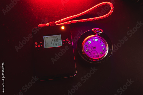 Dosimeter of radioactive radiation next to an old pocket watch with dangerous fluorescent paint. Violet light and green glow of numbers. Dosimetry and search for dangerous objects photo